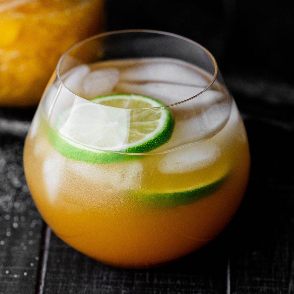 Hero image of a mango drink in a stemless wine glass with a lime wedge.